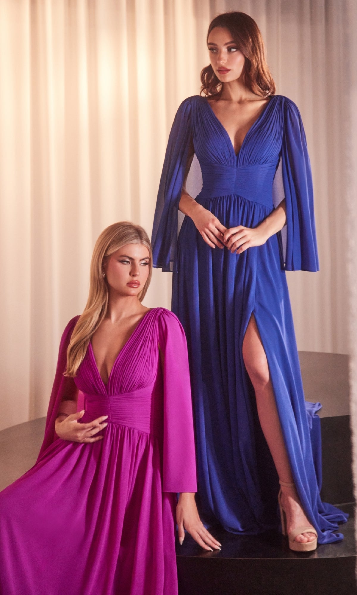 Two women showcase the Ladivine CH028 Ruched Long Chiffon Formal Dress, featuring deep V-necks and pleated accents: one in bright pink sits gracefully, while the other in royal blue stands with a thigh-high slit and open-toe heels.